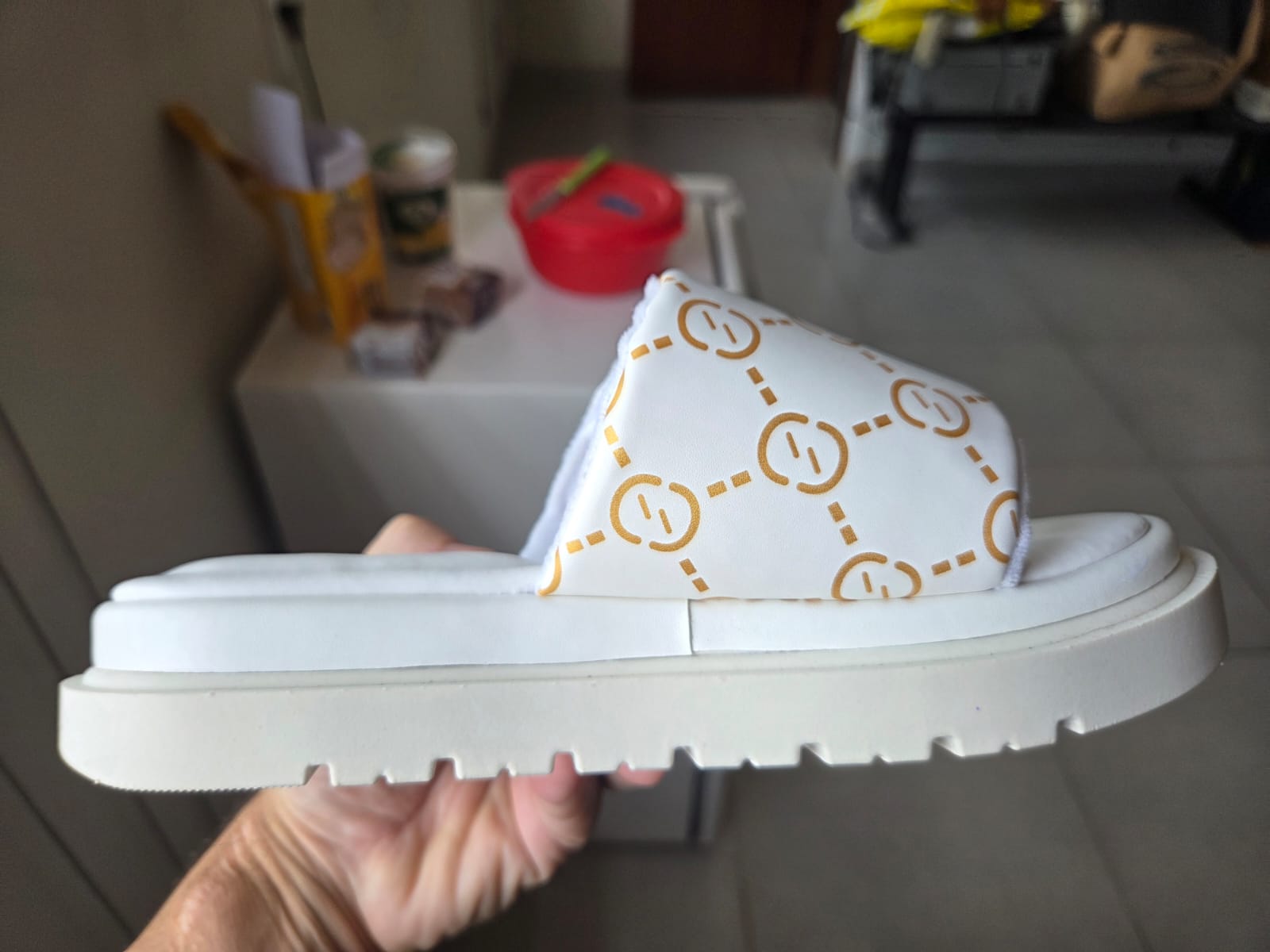 Foto original de chinelo branco com estampa dourada, segurado na mão antes da edição com IA